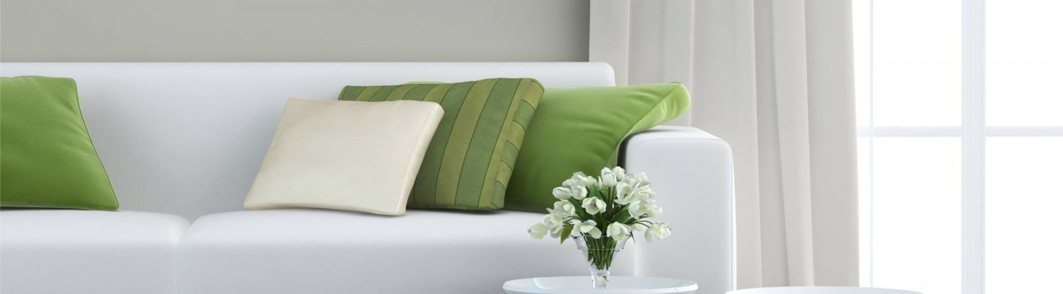 A white couch with green pillows and a vase.